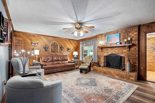 living room with a textured ceiling, wood walls, hardwood / wood-style floors, and a brick fireplace