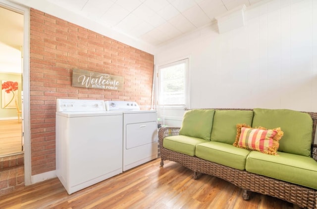 clothes washing area with light hardwood / wood-style floors, brick wall, and washer and dryer