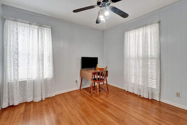 home office featuring wooden walls, light hardwood / wood-style floors, plenty of natural light, and ceiling fan