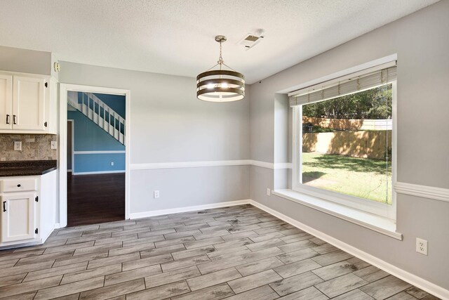 unfurnished dining area with a textured ceiling, light hardwood / wood-style flooring, and a chandelier