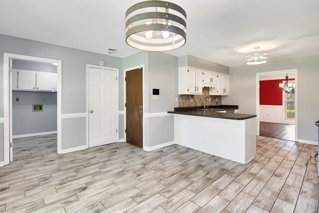 kitchen featuring light wood-type flooring, sink, white cabinetry, kitchen peninsula, and an inviting chandelier