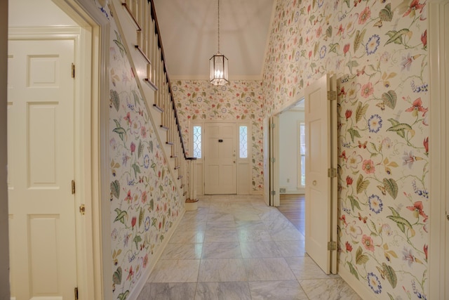 entryway with lofted ceiling, ornamental molding, and an inviting chandelier