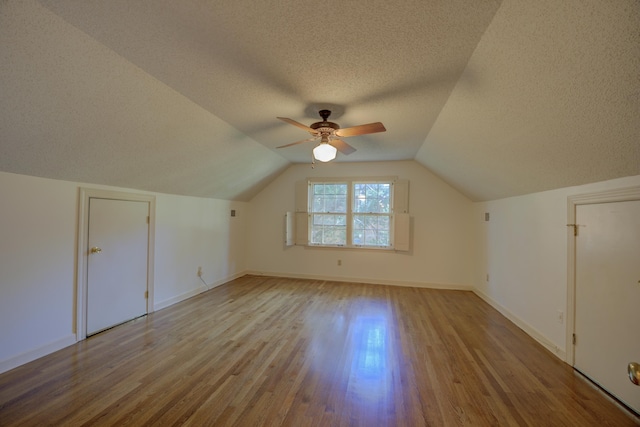 additional living space with light wood-type flooring, vaulted ceiling, a textured ceiling, and ceiling fan