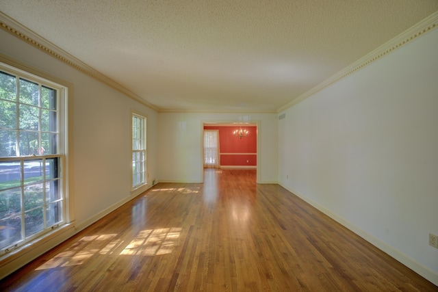 spare room with a textured ceiling, crown molding, hardwood / wood-style floors, and a chandelier