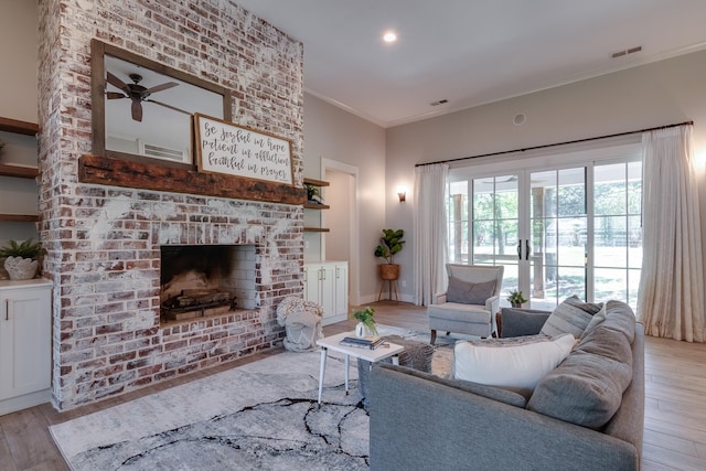 living room featuring ceiling fan, ornamental molding, a brick fireplace, and light hardwood / wood-style floors