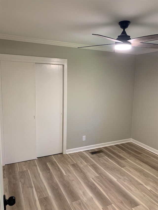 unfurnished bedroom featuring crown molding, ceiling fan, a closet, and wood-type flooring