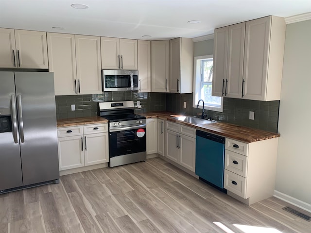 kitchen with wood counters, appliances with stainless steel finishes, backsplash, sink, and light hardwood / wood-style floors