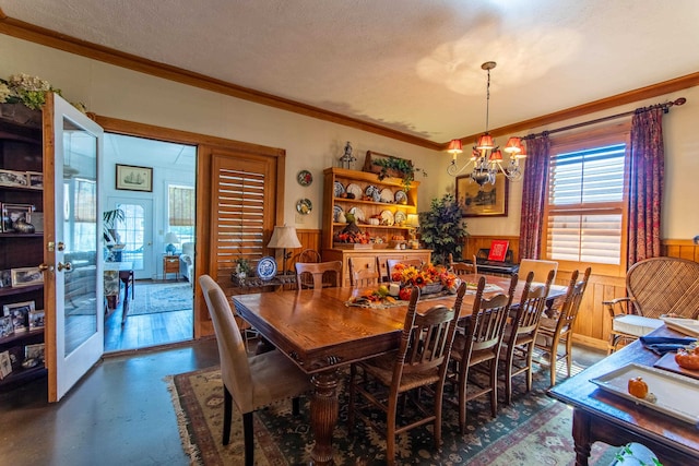 dining room with a textured ceiling, crown molding, wooden walls, and a notable chandelier