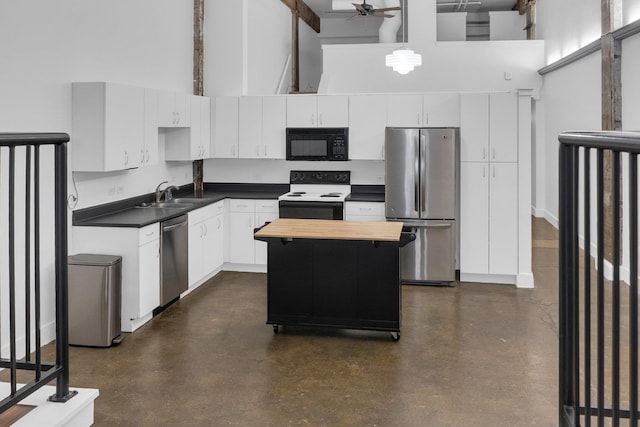 kitchen featuring a center island, sink, white cabinetry, stainless steel appliances, and a towering ceiling