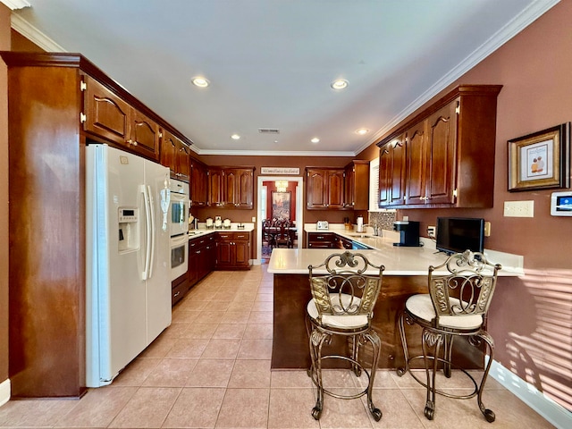 kitchen featuring a breakfast bar, sink, kitchen peninsula, white appliances, and ornamental molding