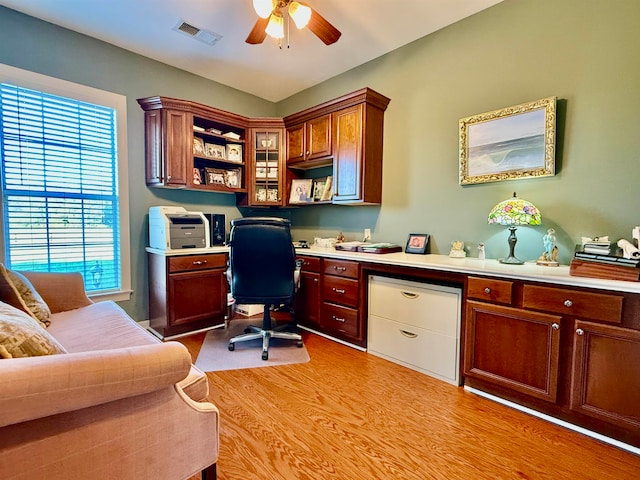 office featuring built in desk, light hardwood / wood-style floors, and ceiling fan