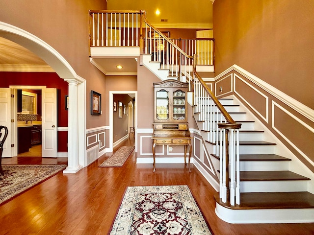 entryway with a towering ceiling, hardwood / wood-style flooring, crown molding, and ornate columns