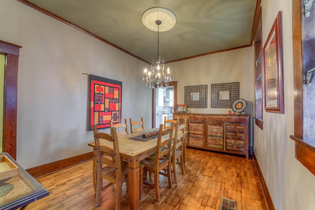 dining area with light hardwood / wood-style floors, ornamental molding, and a chandelier