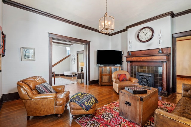 living room with wood-type flooring, a tiled fireplace, a chandelier, and crown molding