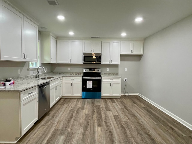 kitchen with appliances with stainless steel finishes, white cabinetry, light stone counters, hardwood / wood-style flooring, and sink