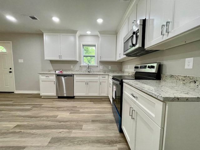 kitchen with white cabinets, light stone countertops, sink, appliances with stainless steel finishes, and light wood-type flooring