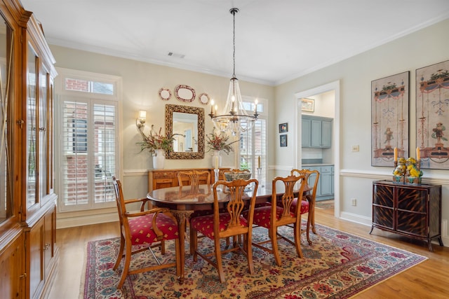 dining space with ornamental molding, a notable chandelier, and light hardwood / wood-style floors