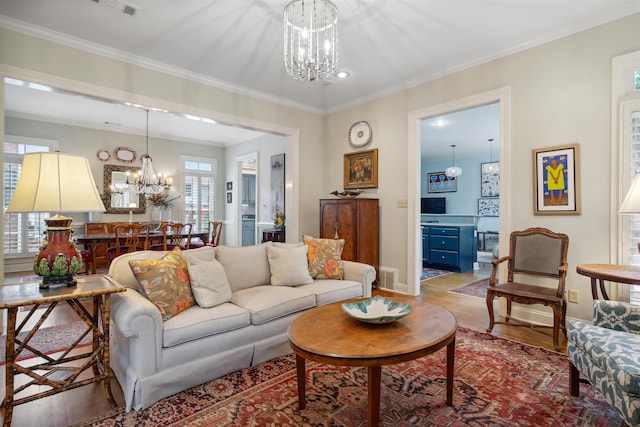 living room with ornamental molding, wood-type flooring, a wealth of natural light, and an inviting chandelier