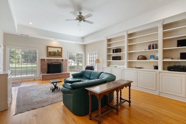 living room featuring ceiling fan, light wood-type flooring, a brick fireplace, and a wealth of natural light