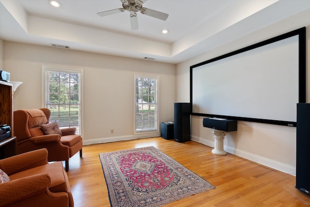 home theater room featuring light hardwood / wood-style floors, a raised ceiling, and ceiling fan