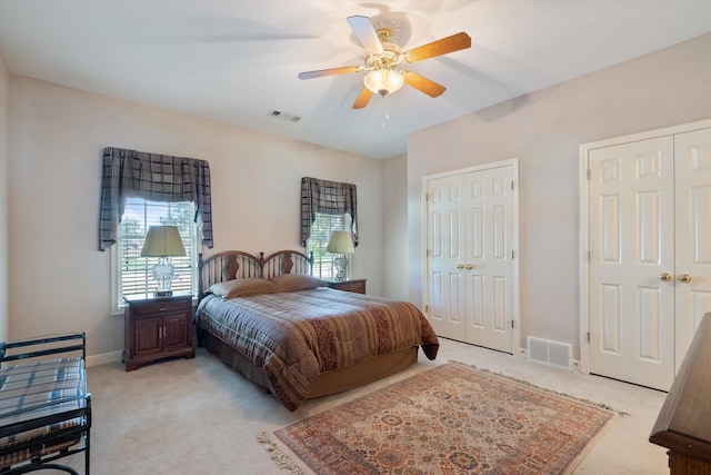 bedroom with two closets, ceiling fan, and light colored carpet