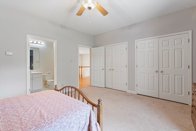 bedroom with ceiling fan, multiple closets, connected bathroom, and light carpet