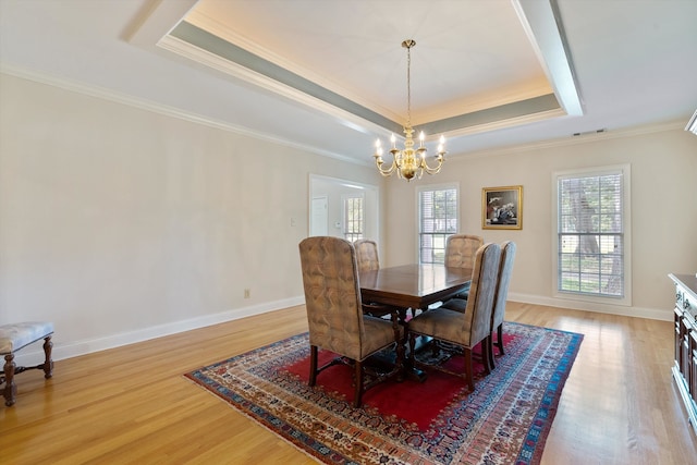 dining room with wood-type flooring, a notable chandelier, a raised ceiling, and crown molding