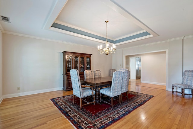 dining space with an inviting chandelier, light hardwood / wood-style flooring, crown molding, and a tray ceiling