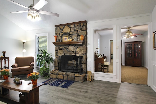 living room with ceiling fan, a stone fireplace, hardwood / wood-style flooring, and lofted ceiling