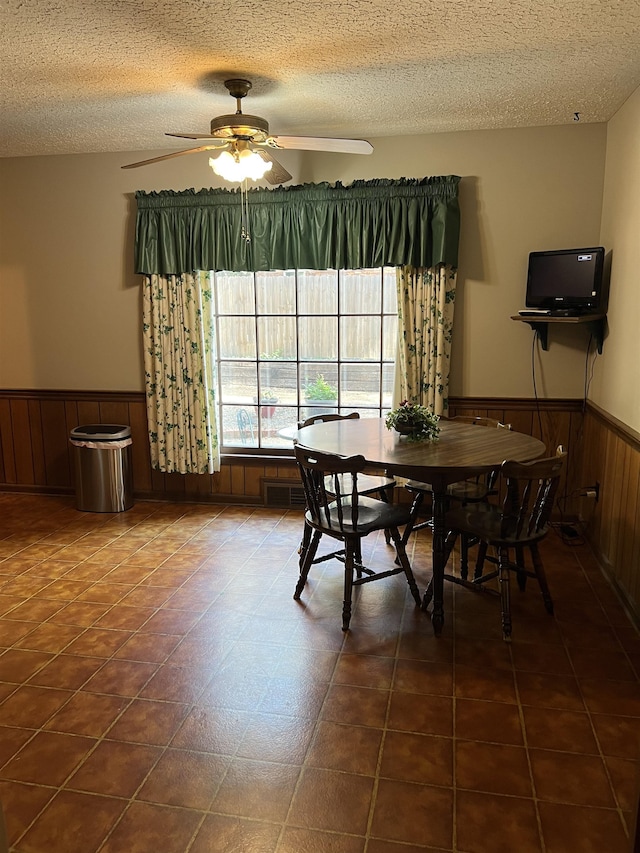 dining space featuring ceiling fan, a textured ceiling, and wood walls