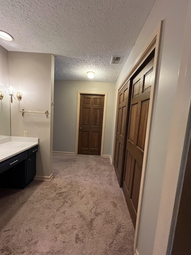 hall with light colored carpet and a textured ceiling