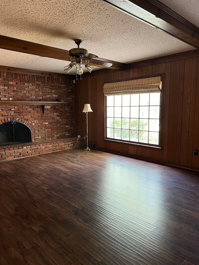 unfurnished living room with wood-type flooring, a textured ceiling, beam ceiling, wooden walls, and ceiling fan