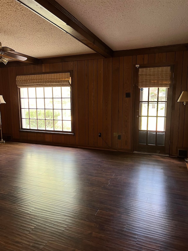 unfurnished room featuring wooden walls, beamed ceiling, ceiling fan, dark wood-type flooring, and a textured ceiling