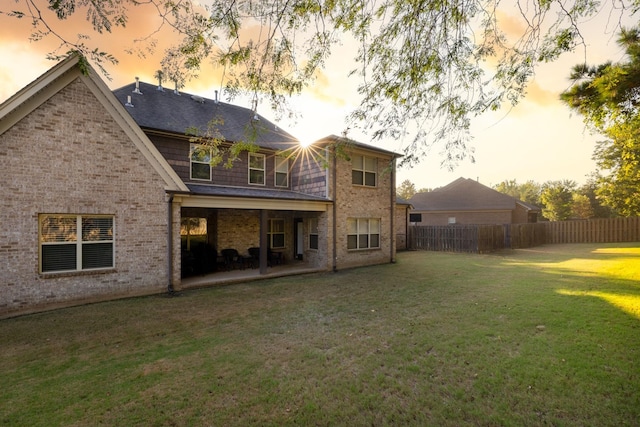 back house at dusk with a lawn and a patio area