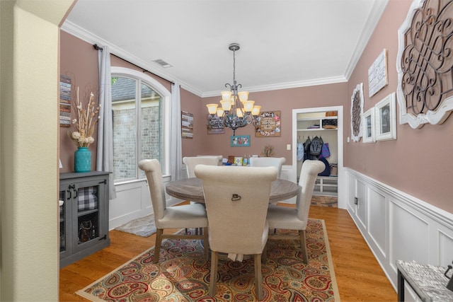 dining space with light wood-type flooring, ornamental molding, beverage cooler, and a chandelier