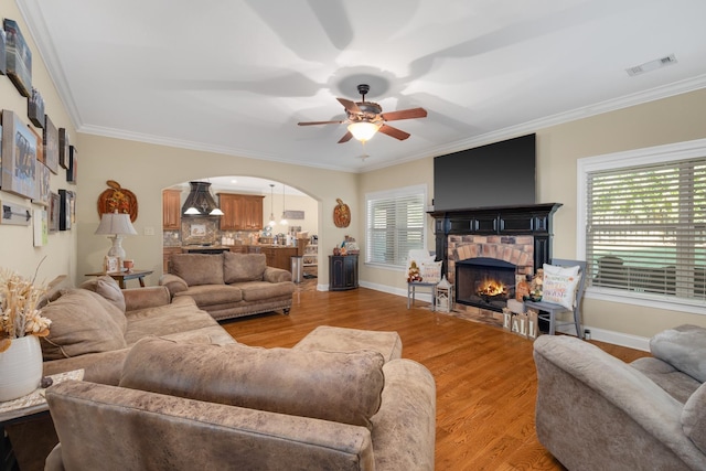 living room with a healthy amount of sunlight, a fireplace, crown molding, and wood-type flooring