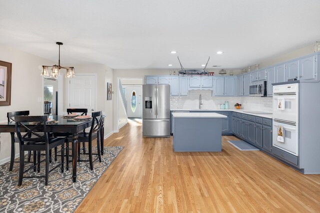 kitchen with light hardwood / wood-style flooring, appliances with stainless steel finishes, hanging light fixtures, tasteful backsplash, and a kitchen island