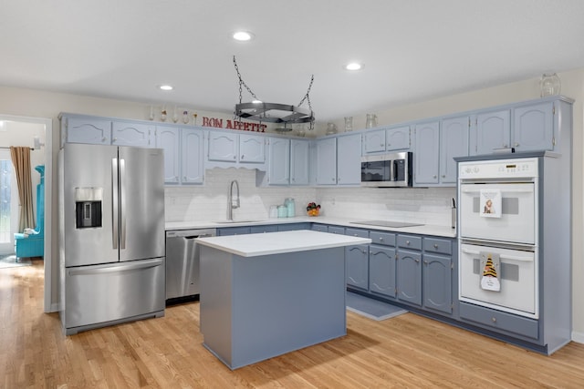 kitchen featuring appliances with stainless steel finishes, a center island, sink, and light wood-type flooring