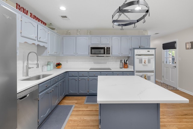 kitchen featuring sink, tasteful backsplash, a kitchen island, stainless steel appliances, and light hardwood / wood-style floors