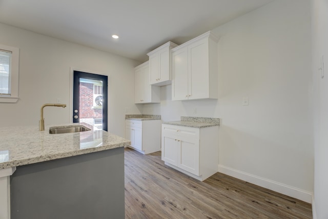 kitchen with light stone countertops, sink, white cabinets, and light hardwood / wood-style floors