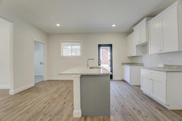 kitchen with an island with sink, sink, white cabinets, and light stone counters