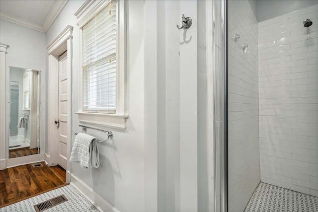 bathroom featuring wood-type flooring, crown molding, and a tile shower