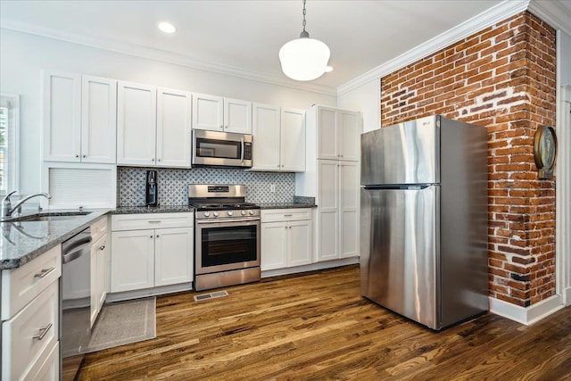 kitchen with appliances with stainless steel finishes, dark stone countertops, dark wood-type flooring, pendant lighting, and sink