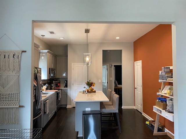 kitchen featuring gray cabinetry, decorative light fixtures, dark wood-type flooring, stainless steel appliances, and a breakfast bar area