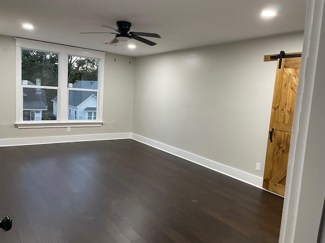 unfurnished room featuring a barn door, dark hardwood / wood-style flooring, and ceiling fan