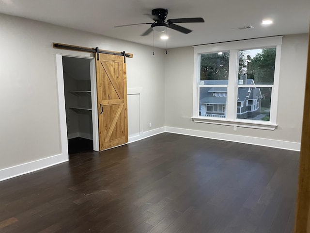 unfurnished room with a barn door, dark hardwood / wood-style floors, and ceiling fan