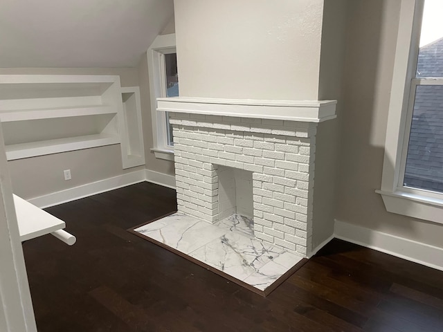 unfurnished living room featuring vaulted ceiling, dark wood-type flooring, and a brick fireplace