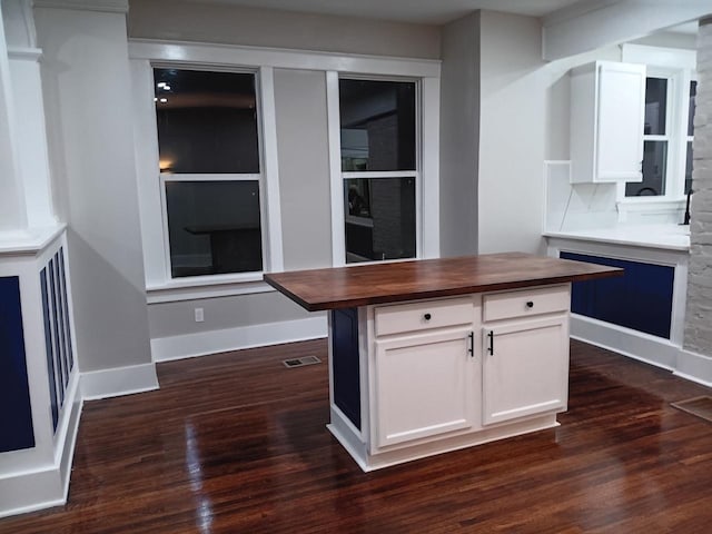 kitchen with a kitchen island, wood counters, dark wood-type flooring, and white cabinets