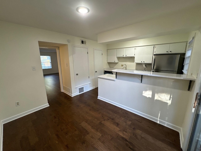 kitchen with dark hardwood / wood-style floors, white cabinets, kitchen peninsula, stainless steel refrigerator, and a kitchen breakfast bar