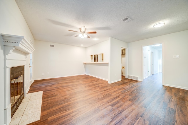 unfurnished living room with ceiling fan, hardwood / wood-style flooring, a textured ceiling, and a tile fireplace